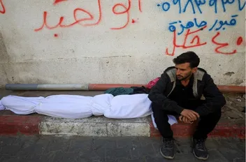 فلسطيني يجلس بجانب جثة شهيد في غزة