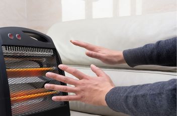 شخص يجلس على الأريكة ويقوم بتدفئة يديه باستخدام مدفئة كهربائية