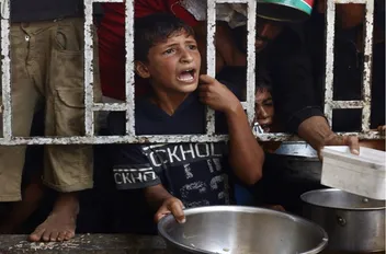 أطفال فلسطينيون يحملون أواني فارغة وهم ينتظرون وجبة طعام في غزة