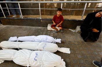 طفل فلسطيني وسيدة يجلسون بالقرب من جثامين شهداء في مستشفى الشفاء في مدينة غزة